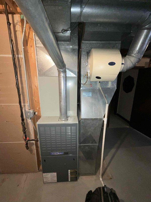 Conducted comprehensive in-home assessment for full HVAC system replacement in residential basement location. Evaluated existing dark gray furnace unit with lower front ventilation grille, extensive silver metal ductwork system with both vertical and horizontal runs, and cream-colored cylindrical humidifier canister mounted to ductwork with dual circular ports. Inspected Bradford White Defender water heater with safety system located in utility area. Assessed basement infrastructure including exposed concrete block foundation walls, wooden framing studs, black electrical wiring, and copper plumbing/gas lines. Documented complete mechanical room layout with concrete slab flooring and current equipment configuration. Gathered specifications and measurements necessary to propose appropriate replacement equipment sized for individual home comfort requirements. Prepared detailed estimate for full system upgrade including furnace, ductwork modifications, and humidification components.