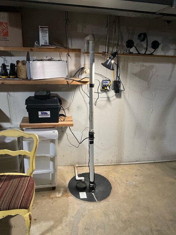 Responded to service call for malfunctioning sump pump system requiring replacement. Assessed existing sump pump installation and associated discharge piping connected to problematic line. Evaluated basement utility area setup including vertical PVC discharge pipe with floor-mounted base plate and wall-mounted shelving infrastructure to determine optimal replacement configuration for reliable water removal system operation.