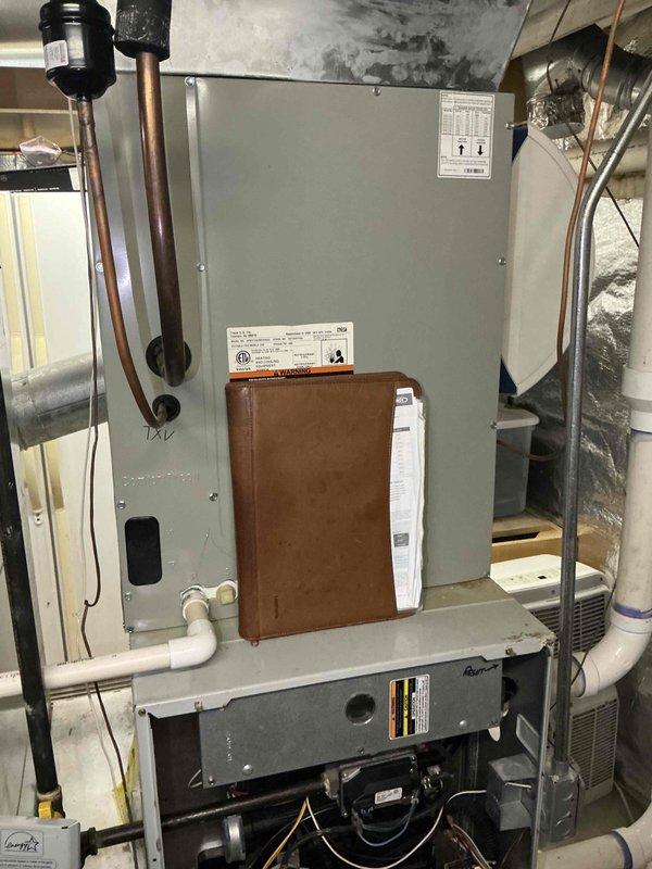 Conducted on-site evaluation of existing HVAC system for replacement estimate. Inspected 25+ year old furnace and air handler unit showing significant age-related wear. Documented current equipment configuration including gray metal furnace with accessible internal components, blower motor assembly, and wiring harnesses. Assessed Carrier-branded air conditioning unit and associated ductwork system. Photographed existing PVC condensate piping, copper refrigerant lines, and metal ductwork connections throughout basement installation. Evaluated overall system layout and clearances for potential replacement equipment. Provided comprehensive assessment of aging equipment condition to support replacement recommendations.