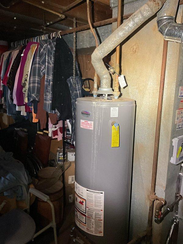 Responded to service call for aging water heater exhibiting active leak and sump pump replacement request. Upon arrival, inspected existing water heater in basement utility area and confirmed deterioration with visible moisture damage. Assessed surrounding plumbing infrastructure including copper supply lines and existing water treatment system. Evaluated sump pump pit location showing evidence of previous water accumulation and floor staining around drainage area. Documented equipment conditions and basement mechanical room layout including overhead PVC discharge piping and flexible connector installations. Provided recommendations for water heater replacement and sump pump upgrade to prevent future water damage and ensure proper basement drainage functionality.