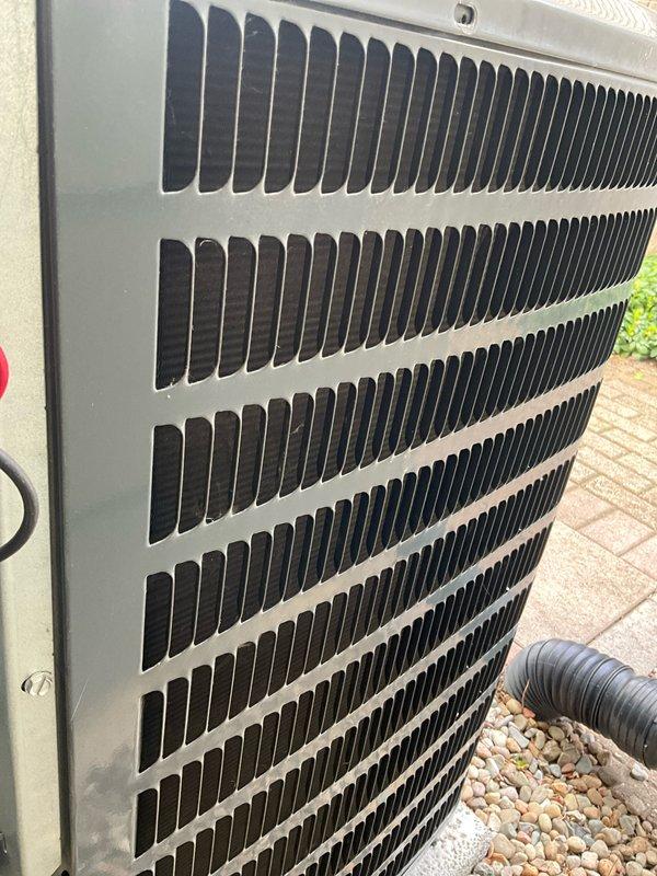Completed comprehensive air conditioning tune-up on a 3-year-old Goodman condenser unit located on exterior paver patio. Performed full system inspection including visual assessment of unit housing, protective grille, and internal components, verified proper airflow through horizontal fin array, checked electrical connections and refrigerant lines, and confirmed unit operational integrity with no visible signs of damage, corrosion, or deterioration noted.