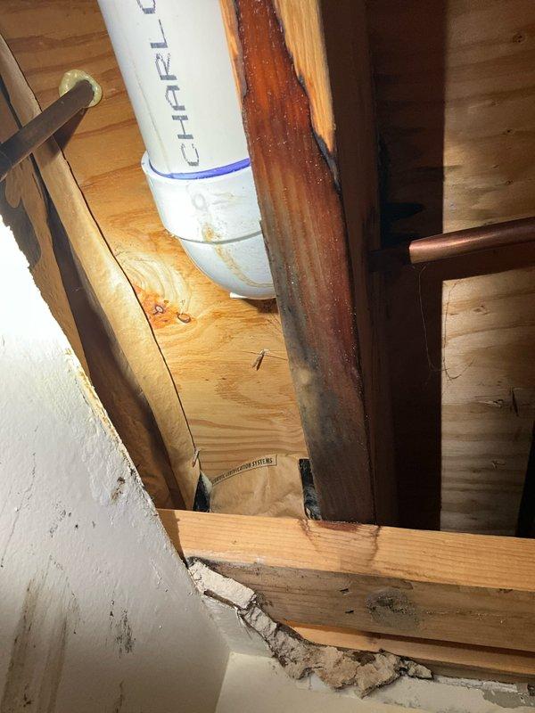 Responded to water leak complaint in basement ceiling directly below bathroom toilet. Upon inspection, discovered active moisture intrusion causing ceiling deterioration, buckling, and significant mold growth in corner areas where walls meet ceiling. Documented extensive black mold colonization and water staining on ceiling surfaces indicating prolonged moisture exposure. Examined basement structural framing and found water damage affecting ceiling joists and drywall integrity. Photographed affected areas including compromised ceiling materials, mold growth patterns, and exposed basement infrastructure. Advised immediate remediation required for mold contamination and recommended toilet seal inspection and replacement as probable source of leak.