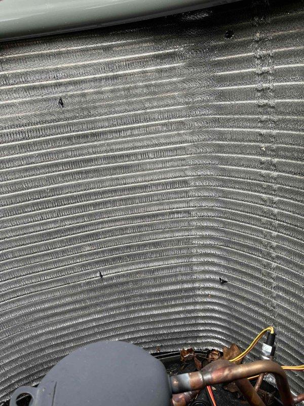 Completed comprehensive BFMA tune-up service on one-year-old HVAC system, including air conditioning system inspection and filter replacement. Inspected evaporator coil assembly and observed dust and debris accumulation on aluminum fins with some discoloration present; verified coil structural integrity remains intact with no damage to fin spacing or copper refrigerant lines. Replaced air filter, confirmed proper system operation, and documented equipment condition with photos showing coil surfaces and refrigerant line connections with brass fittings in satisfactory working order.