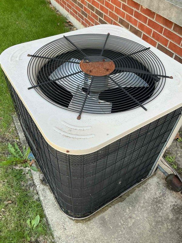 Responded to service call for noisy air conditioning unit on administrative side of commercial property. Upon arrival, inspected outdoor condensing unit and observed signs of normal wear including minor corrosion on fan motor hub and weathering on exterior components. Conducted diagnostic evaluation of unit operation, checking condenser fan motor, compressor operation, and overall system performance. Unit appeared to be functioning within normal parameters during inspection. Documented equipment condition with photos showing residential-style condensing unit installed on concrete pad adjacent to building exterior.
