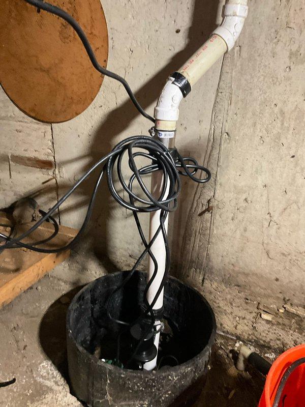 Completed sump pump replacement in crawl space, installing new Aquanot submersible pump system with battery backup capability. Removed existing worn pump unit from basin and installed new green-housed submersible pump with float switch assembly, connecting discharge piping through white PVC system along wall with proper elbow configurations for optimal drainage flow. Installed battery backup system to ensure continued operation during power outages, routing all electrical connections and black power cables along wall and securing properly. Verified pump operation, float switch functionality, and battery backup engagement, confirming system effectively manages groundwater accumulation and provides reliable emergency backup protection.