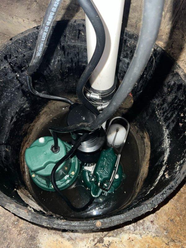 Completed sump pump replacement in crawl space, installing new Aquanot submersible pump system with battery backup capability. Removed existing worn pump unit from basin and installed new green-housed submersible pump with float switch assembly, connecting discharge piping through white PVC system along wall with proper elbow configurations for optimal drainage flow. Installed battery backup system to ensure continued operation during power outages, routing all electrical connections and black power cables along wall and securing properly. Verified pump operation, float switch functionality, and battery backup engagement, confirming system effectively manages groundwater accumulation and provides reliable emergency backup protection.