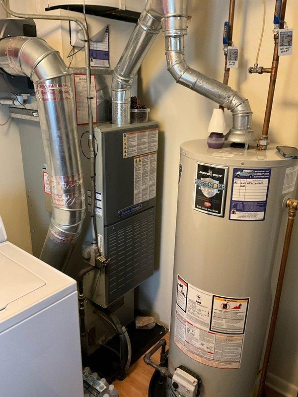 Completed comprehensive air conditioning tune-up for new client on residential system. Performed thorough inspection of outdoor condenser unit, noting dust and debris accumulation on coil fins, and inspected indoor furnace components and air handler. Evaluated system operation, checked refrigerant lines and connections, assessed compressor function, and verified proper electrical connections. Documented equipment condition with photographs showing outdoor unit with circular coil configuration and indoor HVAC equipment including furnace and associated ductwork. System operational at completion of service visit.