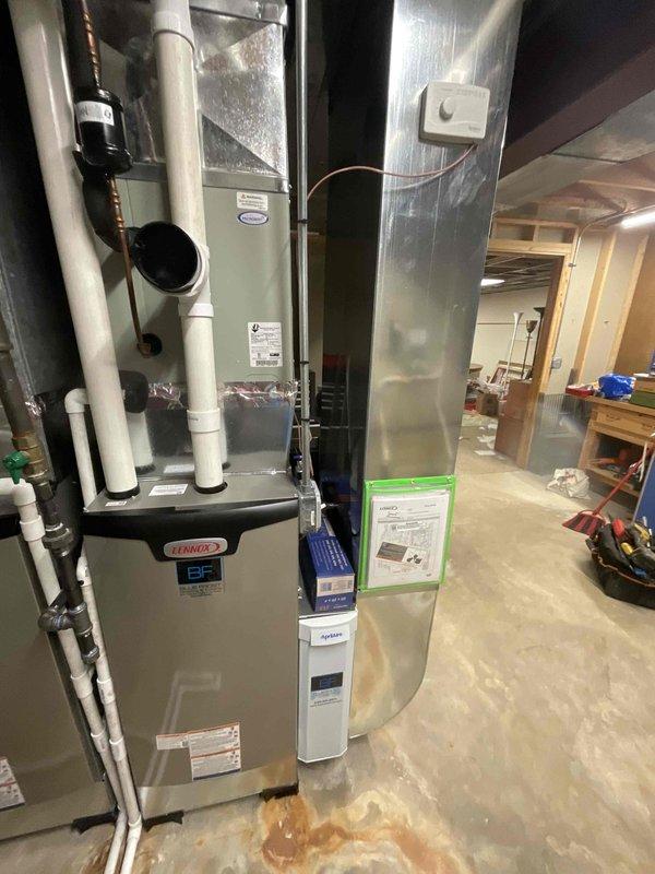 # HVAC Install - Furnace

Completed installation of Lennox furnace system in basement mechanical room, replacing existing heating equipment. Installed new beige Lennox furnace unit with proper vertical mounting and secured all manufacturer specification labels and safety documentation to unit front panel. Connected white PVC venting system along left side of unit with both vertical and horizontal runs to ensure proper exhaust ventilation. Fabricated and installed silver metal supply plenum at furnace top, connecting to existing ductwork distribution system. Installed sheet metal return air duct on right side of furnace with white access panel for filter maintenance and system inspection. Routed electrical connections to furnace and mounted white control unit to ductwork for system operation. All ductwork connections sealed and secured to prevent air leakage. Verified proper clearances around unit for service access and safety compliance. System tested and confirmed operational.