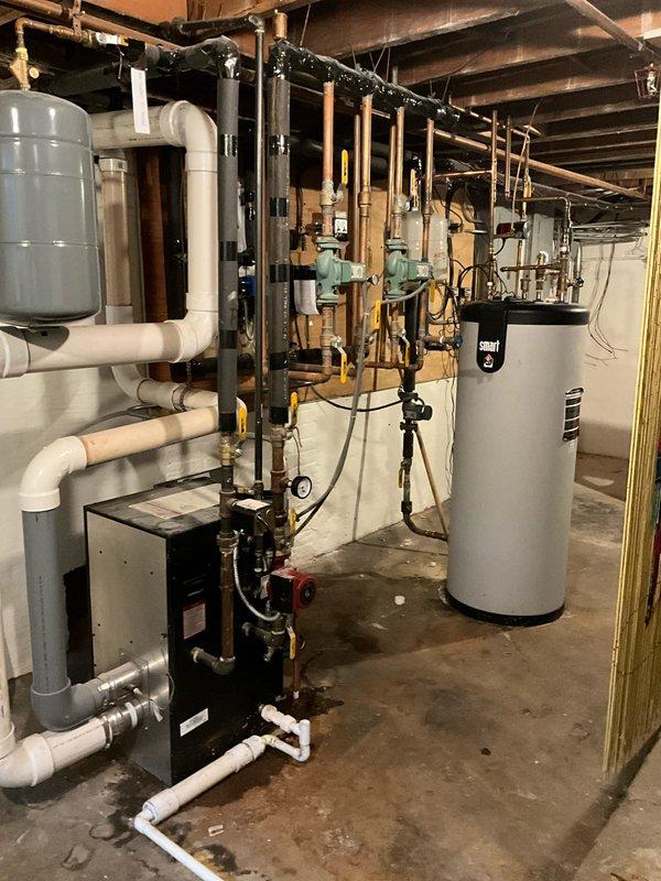 Responded to after hours service call for boiler system evaluation. Upon arrival, conducted comprehensive inspection of hydronic heating system including black boiler unit, gray expansion tank, white PVC piping network, green circulation pumps, copper gas lines, and associated mechanical components in basement mechanical room. Documented existing equipment configuration and current operational status through photographic assessment of complete installation including all piping manifolds, valves, controls, and safety devices. System shows standard residential hydronic heating setup with properly mounted expansion tank, circulation pumps, and water heater integration.