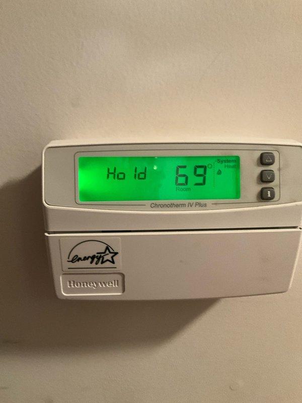 Responded to after-hours heating system failure on 20+ year old residential HVAC unit. Upon arrival, inspected Honeywell Chronotherm IV Plus programmable thermostat showing hold mode at 69°F and conducted visual assessment of blower assembly. Documented significant dust accumulation on squirrel cage blower wheel blades and housing, which can restrict airflow and cause system performance issues. Photographed blower wheel assembly showing dusty metal blades and central hub with motor coupling, as well as thermostat display for diagnostic reference.