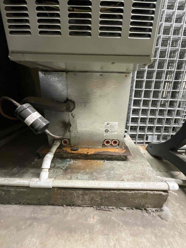 Conducted comprehensive full system HVAC estimate at residential property with brick exterior. Evaluated existing dual outdoor condenser units positioned on ground-level installation adjacent to building foundation, with visible signs of aging including rust staining and corrosion on mounting surfaces and connection points. Assessed condensate drainage system consisting of white PVC piping in U-shaped configuration and metallic flex connectors showing deterioration. Documented current equipment condition, noting surface wear on concrete pad, discoloration around pipe connections, and overall system age to provide accurate replacement recommendations for complete heating and cooling system upgrade.