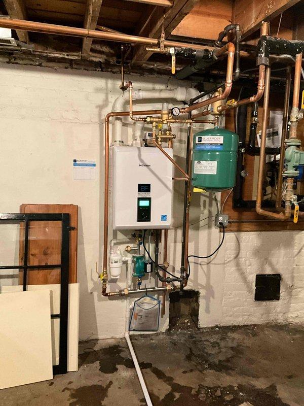 # HVAC Install - Boiler

## Work Performed

Completed full boiler replacement with installation of Navien NHB-150 tankless boiler system. Removed existing boiler unit and installed new wall-mounted tankless boiler on concrete block wall in basement mechanical room. 

Installed complete copper piping network with brass fittings and shut-off valves to connect tankless boiler to existing indirect water tank. Configured system for two-zone heating operation as specified. Mounted expansion tank on wall adjacent to main unit and integrated into system with proper connections.

Installed Navien manifold kit to facilitate multi-zone distribution. Added circulation pump at floor level to ensure proper flow throughout system. Ran PVC venting pipes from unit through ceiling for exhaust and combustion air intake per manufacturer specifications.

Installed condensate neutralizer to treat acidic condensate discharge from high-efficiency boiler operation, ensuring compliance with local codes. Integra