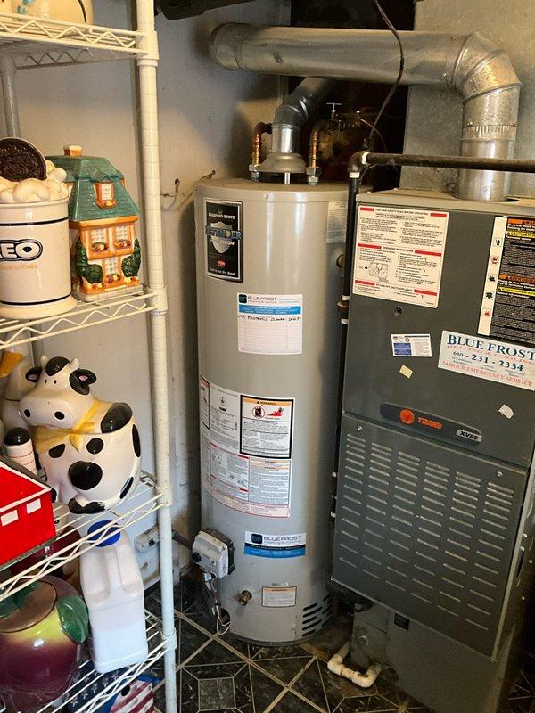 Responded to after hours call for non-operational water heater at residential property. Upon arrival, inspected 15-year-old cylindrical water heater unit located in basement utility area adjacent to HVAC furnace system. Performed visual assessment of water heater exterior, piping connections, and surrounding mechanical equipment. Documented equipment condition through photography showing water heater installation, associated ductwork, metal piping connections at top of unit, and overall mechanical room configuration. Updated customer contact information in system for ongoing communication regarding repair options and next steps.