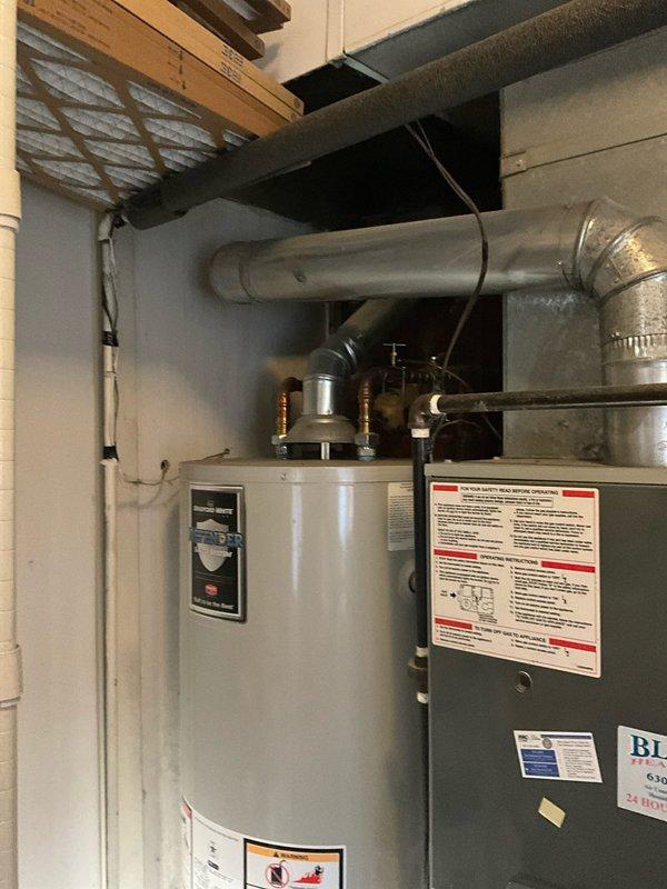 Responded to after hours call for non-operational water heater at residential property. Upon arrival, inspected 15-year-old cylindrical water heater unit located in basement utility area adjacent to HVAC furnace system. Performed visual assessment of water heater exterior, piping connections, and surrounding mechanical equipment. Documented equipment condition through photography showing water heater installation, associated ductwork, metal piping connections at top of unit, and overall mechanical room configuration. Updated customer contact information in system for ongoing communication regarding repair options and next steps.
