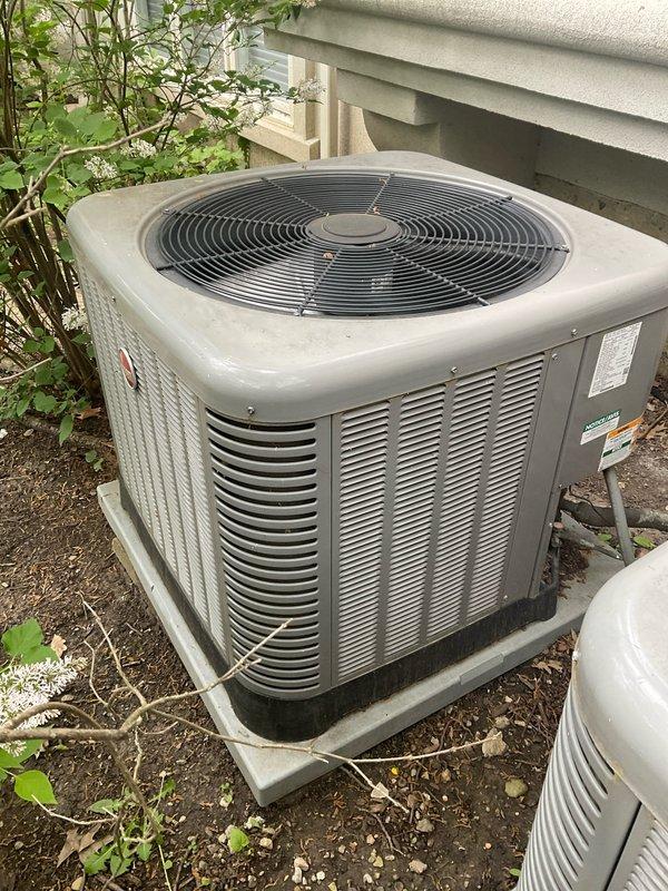 Completed non-member maintenance tune-up on two air conditioning systems. Investigated reported burning odor occurring when heat activates for second floor. Inspected 10+ year old Goodman outdoor condensing unit model RAJ348AJ1NA manufactured 04/2018. Performed comprehensive system evaluation including visual inspection of condenser cabinet, fan operation, refrigerant lines, and electrical connections. Verified proper airflow through louvered panels and assessed condenser fan functionality. Checked manufacturer specifications and operational parameters. Unit positioned on composite pad with adequate clearance from vegetation. Documented equipment condition and specifications for service records. Both systems evaluated for safe operation and performance efficiency.