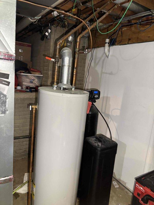 Responded to after hours service call for water heater system inspection. Upon arrival, documented existing basement mechanical room configuration including water heater installation with expansion tank, copper supply lines, and associated plumbing connections. Water softener system with digital display panel observed operating adjacent to water heater unit. Verified proper clearances around equipment and documented current installation conditions including exposed ceiling utilities, HVAC ductwork, electrical conduits, and plumbing distribution lines throughout mechanical space. All equipment photographed for service records showing white cylindrical pressure tank, brass fittings, copper piping connections, and water treatment system. No immediate repairs required at time of inspection.
