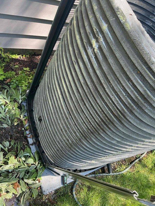 Completed comprehensive BFMA tune-up service on residential air conditioning system with equipment over 2 years old, scheduled for mid-morning arrival with 30-minute advance notice. Performed thorough inspection of outdoor condenser unit, examining cylindrical heat exchanger coil with horizontal fins for proper condition and airflow. Assessed insulation material around refrigerant lines and protective cage structure surrounding the unit. Documented equipment condition through photographic evidence showing condenser positioning on concrete pad, fin spacing and cleanliness, and overall system installation against building exterior with proper clearances from landscaping.