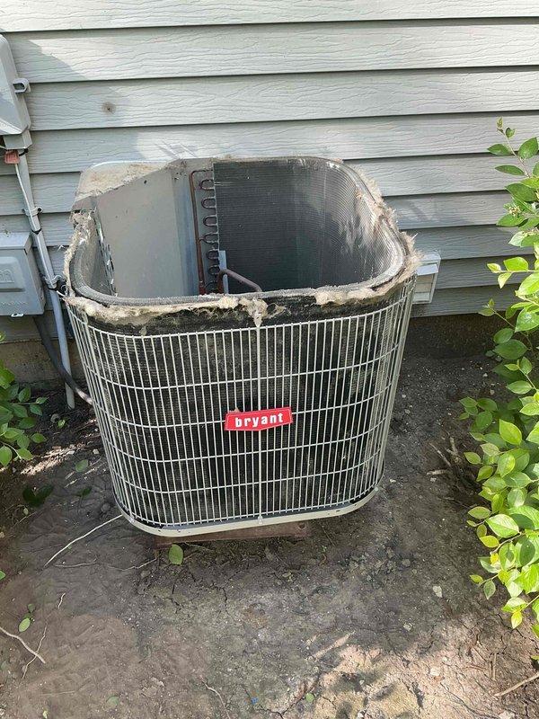 Completed comprehensive BFMA tune-up service on 9-year-old Bryant air conditioning system. Upon arrival, discovered outdoor condenser unit in severely deteriorated condition with top cover completely missing, exposing internal components including fan motor assembly. Noted significant weathering damage with compromised housing, jagged edges around top opening, deteriorating insulation material, and dark staining throughout unit indicating extensive rust and possible mold accumulation. Documented damaged protective grille and exposed mechanical components. Unit positioned on weathered, cracked concrete pad with vegetation growth nearby. Performed standard AC tune-up procedures including system inspection, operational assessment, and photographic documentation of equipment condition. Advised customer of critical safety concerns and structural damage requiring immediate attention for proper system function and efficiency.