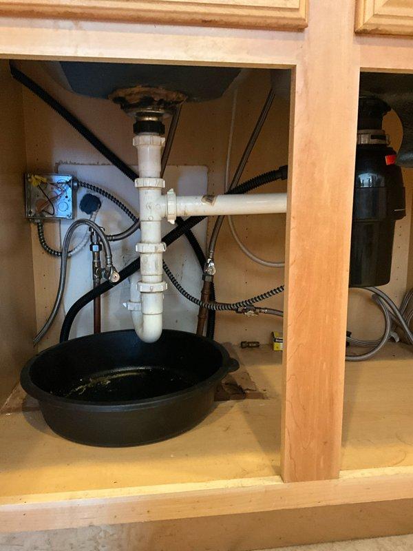 Responded to service call for clogged kitchen sink with reported leaking beneath cabinet. Upon arrival, inspected under-sink plumbing assembly and garbage disposal unit. Identified blockage in drain line causing backup and slow drainage. Cleared obstruction from disposal and drain system using appropriate methods. Tested disposal operation and verified reset button functionality. Inspected all PVC drain connections, P-trap assembly, and supply lines for source of reported leak. Tightened fittings as needed and confirmed proper drainage flow. Verified all connections were secure with no active leaks present. System restored to full working order with proper drainage confirmed.