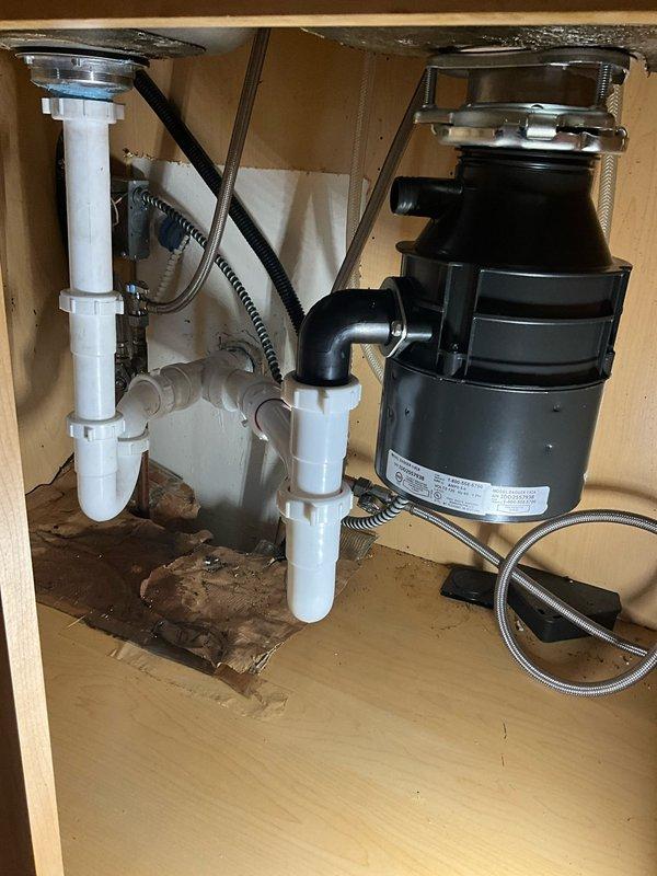 Responded to a kitchen drainage blockage by completely removing and replacing the under-sink plumbing system. Removed all existing drainage lines, including the old garbage disposal unit. Attempted to clear the branch line blockage using a drain rod. Installed a new 1/2 horsepower garbage disposal, new basket strainer, dishwasher tailpiece, and two new P-traps to restore proper drainage function. Deployed air mover equipment to address moisture concerns from previous leaking issues evident on the cabinet floor.