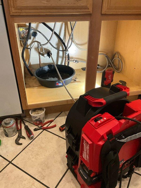 Responded to a kitchen drainage blockage by completely removing and replacing the under-sink plumbing system. Removed all existing drainage lines, including the old garbage disposal unit. Attempted to clear the branch line blockage using a drain rod. Installed a new 1/2 horsepower garbage disposal, new basket strainer, dishwasher tailpiece, and two new P-traps to restore proper drainage function. Deployed air mover equipment to address moisture concerns from previous leaking issues evident on the cabinet floor.