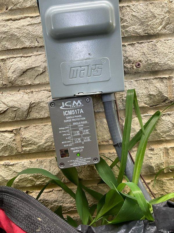 Installed ICM517A single-phase surge protection device on exterior wall to protect HVAC system from electrical surges and voltage spikes. Unit was properly mounted to brick veneer with weatherproof cover securing upper connection point, and both LED indicators confirmed operational status upon completion.