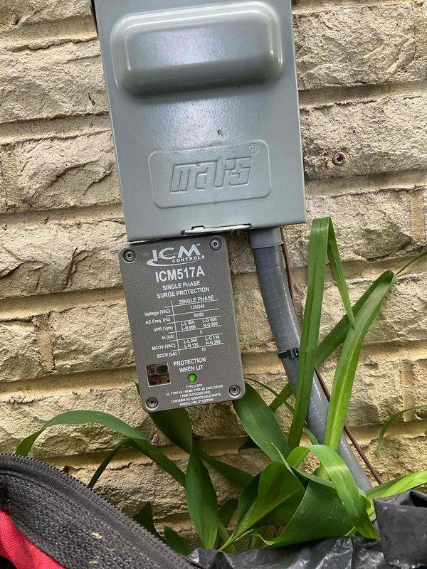Installed ICM517A single-phase surge protection device on exterior wall to protect HVAC system from electrical surges and voltage spikes. Unit was properly mounted to brick veneer with weatherproof cover securing upper connection point, and both LED indicators confirmed operational status upon completion.