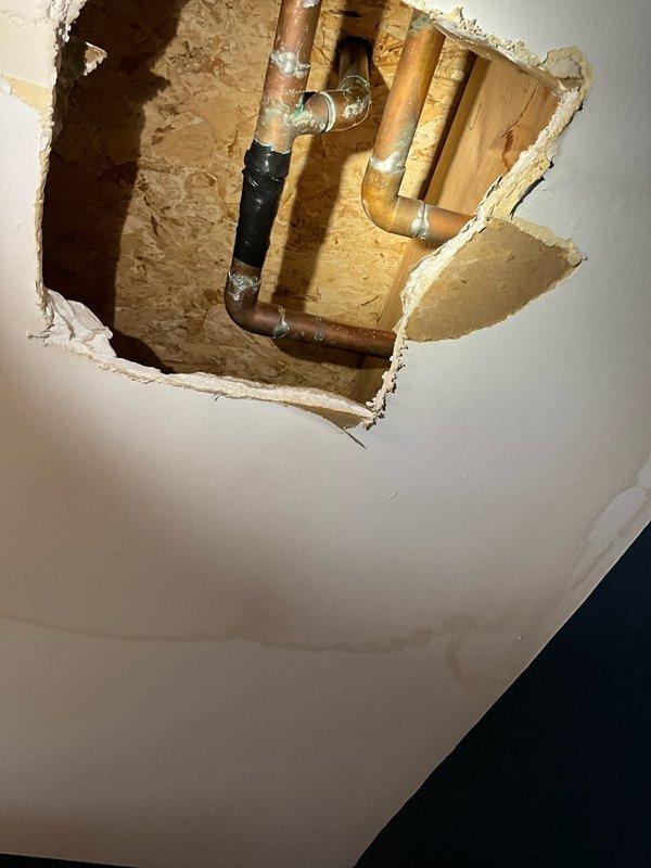 Responded to water leak originating from upstairs bathroom and penetrating into downstairs bathroom ceiling. Upon investigation, identified failed copper water supply line at T-fitting junction between floor joists. Created ceiling access opening to expose plumbing infrastructure and locate source of leak. Repaired compromised T-connection on copper supply line, verified system integrity, and confirmed no additional leaks present. All water supply lines tested and restored to proper working condition.