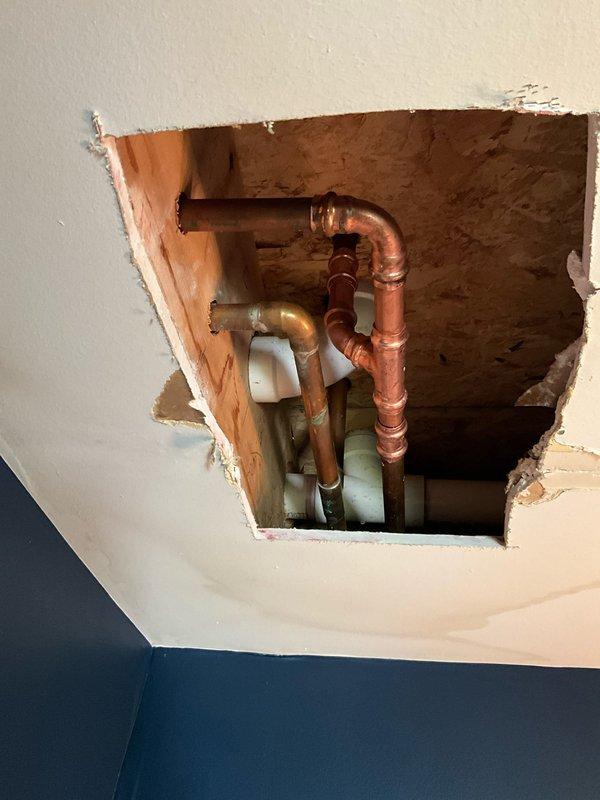Responded to water leak originating from upstairs bathroom and penetrating into downstairs bathroom ceiling. Upon investigation, identified failed copper water supply line at T-fitting junction between floor joists. Created ceiling access opening to expose plumbing infrastructure and locate source of leak. Repaired compromised T-connection on copper supply line, verified system integrity, and confirmed no additional leaks present. All water supply lines tested and restored to proper working condition.