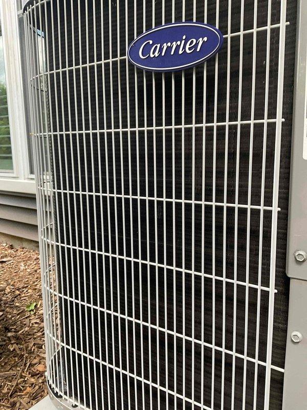 Responded to service call for Carrier outdoor condensing unit reported to have shifted off base with piping concerns. Upon arrival, performed visual inspection of unit and surrounding area. Condenser unit found positioned on ground mulch bed adjacent to structure with white vinyl siding. Inspected unit cage, coil fins, and refrigerant line connections for displacement, damage, or stress points. Protective grille and internal components examined for proper alignment and structural integrity. Unit appears stable with no visible damage to cabinet, coil assembly, or piping connections observed during inspection.