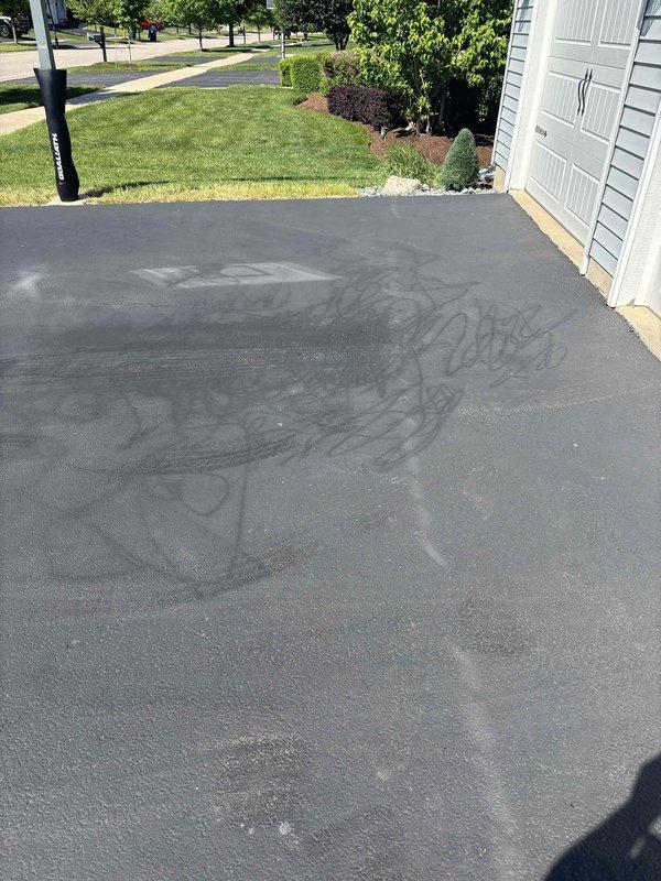 Responded to callback for driveway staining concerns following initial service visit. Upon arrival, assessed asphalt driveway surface showing darker sealant patches and irregular color variations across the pavement. Deployed power washing equipment to address staining and surface discoloration as requested. Treated affected areas where sealant material had created uneven appearance and glossy patches contrasting with weathered concrete sections. Completed surface cleaning procedures and documented final condition showing uniform dark gray asphalt surface with typical tire marks and scuff patterns consistent with normal driveway use.