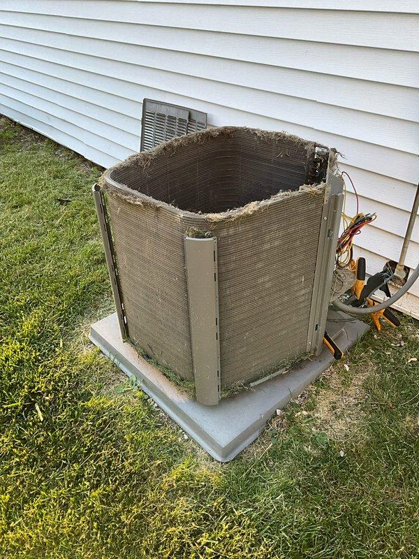 Completed comprehensive BFMA tune-up on residential air conditioning system, arriving after 5 PM per customer's work schedule. Performed standard maintenance protocol including inspection of outdoor condenser unit, which revealed significant damage with top protective grille and cover completely missing, exposing interior coil structure. Noted condenser coil showing weathered appearance with frayed edges where protective casing has deteriorated. Inspected refrigerant lines, electrical connections, and service valves with yellow and red components, confirming all connections secure. Verified electrical disconnect box mounted on exterior wall functioning properly with conduit connections intact. Documented unit condition with photographs for service records, noting equipment positioned on concrete pad with adequate clearance from structure.
