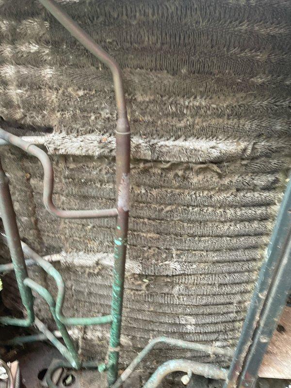 Completed comprehensive BFMA tune-up service on 12+ year old air conditioning system as first stop of the day. Performed standard AC maintenance protocol including system inspection, replaced disposable pleated air filter, and assessed evaporator coil condition. Upon inspection, discovered evaporator coils heavily contaminated with accumulated dust and debris buildup, significantly restricting airflow and reducing system efficiency. Noted copper refrigerant lines showing surface oxidation and greenish patina formation, indicating age-related deterioration. The dense layer of particulate matter coating the coil fins and accordion-style surfaces demonstrated extended operation without regular maintenance. White residue streaking observed on horizontal coil sections suggests possible condensate drainage issues or mineral deposits. The substantial contamination level found throughout the coil assembly will impair heat transfer capability and increase compressor workload if not addressed. D