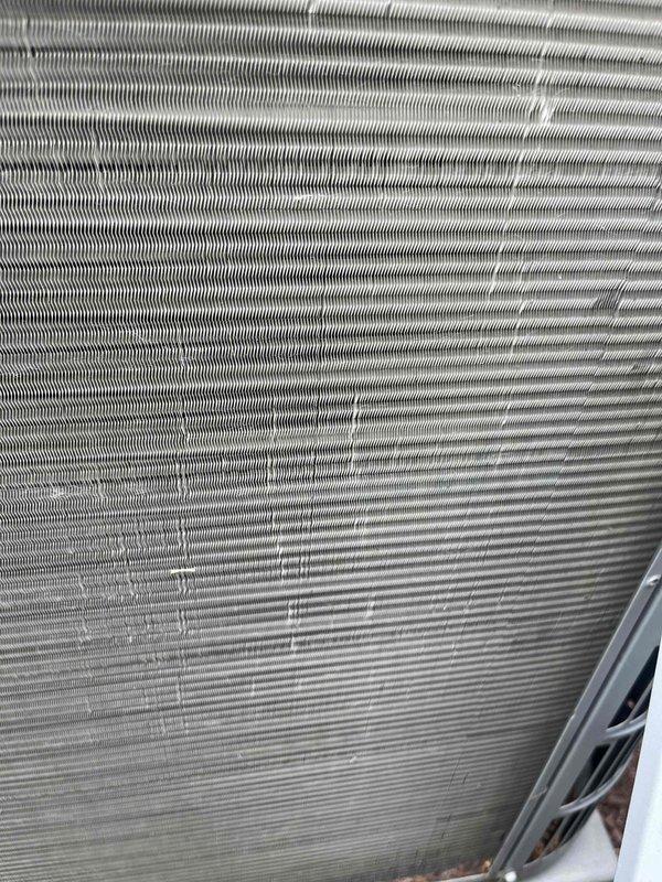 Completed BFMA preventive maintenance tune-up on 8-year-old air conditioning system. Performed comprehensive inspection of evaporator and condenser coils, noting brownish discoloration and oxidation on condenser fins indicating dirt accumulation and minor corrosion. Observed slight fin deformation in center section of coil assembly, likely from previous impact or stress. Documented coil condition with photographs showing varying cleanliness levels across heat exchanger surfaces. System operational at time of inspection.