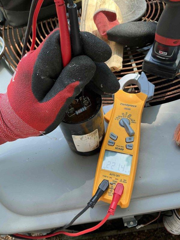 Completed comprehensive AC tune-up on 24+ year old outdoor condensing unit. Removed accumulated organic debris, dirt, and plant material from cooling fins and top surface. Performed electrical diagnostics including capacitor testing with digital multimeter to verify proper system operation and component functionality.