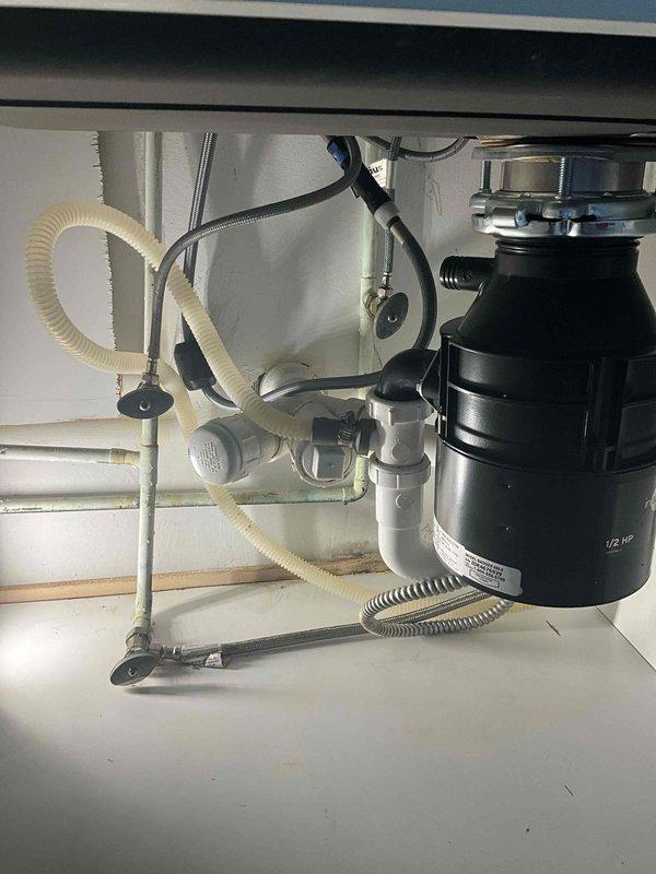 Completed installation of new garbage disposal unit beneath kitchen sink. Mounted black disposal unit to sink drain with chrome mounting hardware and connected to existing PVC drain line configuration. Installed corrugated dishwasher drain hose connection and verified proper drainage flow through P-trap assembly. Secured all plumbing connections, tested unit operation, and confirmed leak-free installation.