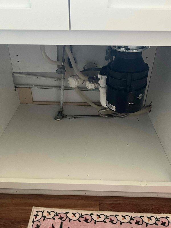 Completed installation of new garbage disposal unit beneath kitchen sink. Mounted black disposal unit to sink drain with chrome mounting hardware and connected to existing PVC drain line configuration. Installed corrugated dishwasher drain hose connection and verified proper drainage flow through P-trap assembly. Secured all plumbing connections, tested unit operation, and confirmed leak-free installation.