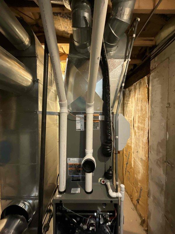 Completed full HVAC system installation in basement mechanical room consisting of EL15KC1-048 air conditioning unit paired with CK40Ct-48C coil and EL297110V48CK high-efficiency 97% AFUE two-stage furnace with 110,000 BTU capacity. Installed AA1210 filter rack assembly and integrated existing thermostat with new equipment. Routed white PVC condensate drain lines and venting from furnace through confined space between framed walls, connecting to flexible ductwork system running through ceiling joists. Installed 40-amp two-pole Siemens circuit breaker for electrical service to outdoor condensing unit. Connected copper refrigerant lines between indoor coil and outdoor unit. Secured all ductwork transitions and verified proper airflow routing through basement installation area. Tested system startup, verified proper operation of both heating and cooling cycles, and confirmed all safety controls functioning correctly.