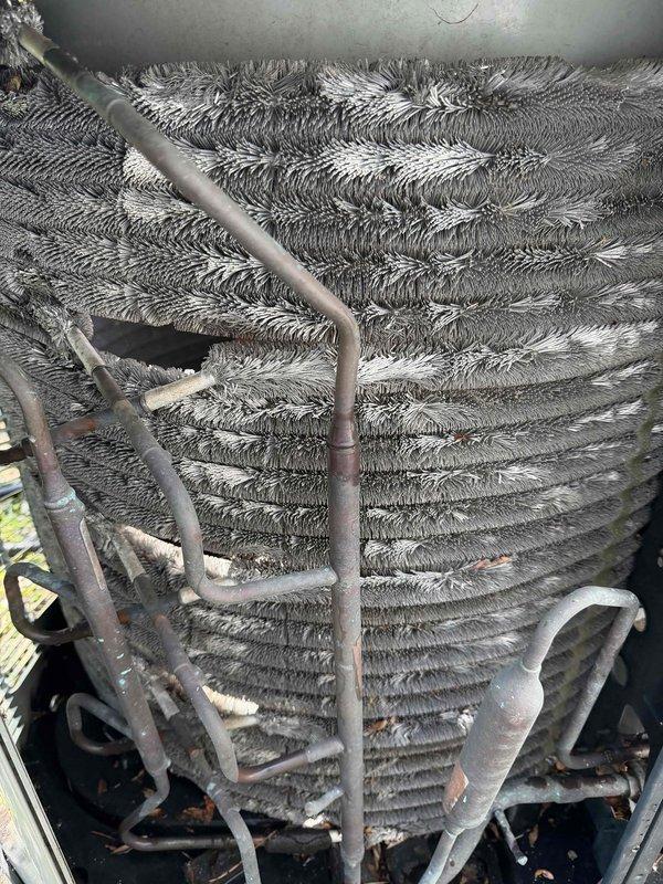 # HVAC Maintenance - BFMA Tune Up Completed

Performed comprehensive BFMA tune-up service on 14+ year old residential air conditioning system during afternoon service window. Upon arrival, conducted thorough visual inspection of outdoor condenser unit, which revealed significant deterioration of protective coil wrap with multiple tears, gaps, and heavy soiling from prolonged environmental exposure. Base plate exhibited moderate rust and corrosion at mounting points and edges, consistent with age of equipment.

Inspected condenser coil assembly and identified substantial accumulation of dirt, dust, and debris throughout fin surfaces, creating restricted airflow conditions. Coil fins displayed typical oxidation and contamination buildup in horizontal striped pattern across heat exchange surfaces. Verified refrigerant line connections and observed normal oxidation on copper piping consistent with outdoor installation age.

Examined electrical components including capacitor and control box