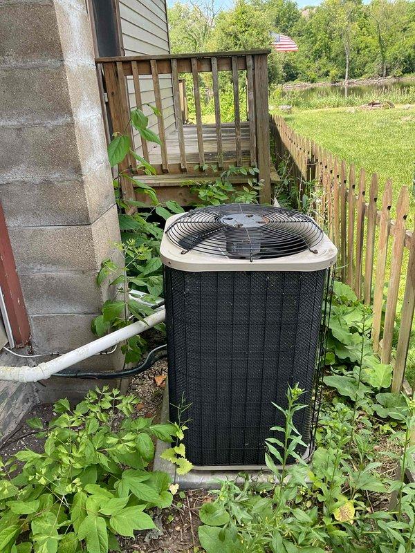 Completed comprehensive BFMA tune-up service on 20-year-old outdoor air conditioning condenser unit. Performed standard maintenance protocol including system inspection, component testing, and operational verification. Unit was accessed despite significant vegetation overgrowth around the base and perimeter; condenser found in operational condition with protective mesh covering intact and properly secured to wire grid framework.