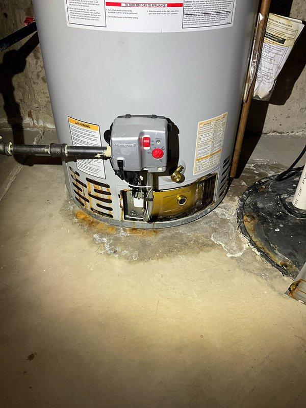 Responded to service call for non-operational water heater with reported water leak. Upon inspection, found active water pooling at base of unit on concrete floor near drain, with visible moisture damage and deterioration to surrounding concrete surface including cracking and efflorescence. Examined gas control assembly, copper piping connections, and relief valve for signs of failure. Water heater showing age-related wear with compromised tank integrity indicated by standing water at base. Documented conditions with photographs showing extent of leak, floor damage, and unit configuration. Assessed unit as requiring replacement due to tank failure rather than repairable component issue.