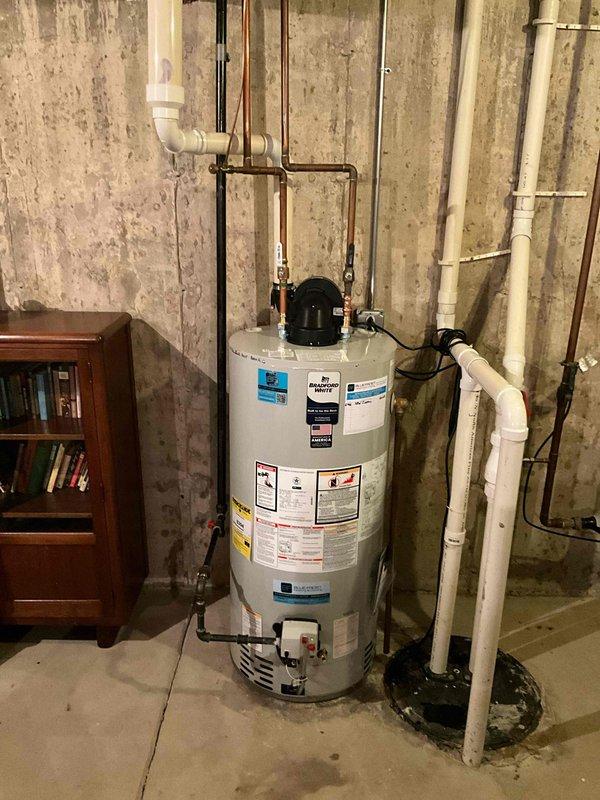 Removed existing water heater from basement utility area and properly disposed of old unit. Installed new 50-gallon natural gas Bradford White power vent water heater with 6-year tank warranty and 1-year parts and labor warranty. Modified and connected gas supply line with appropriate fittings to ensure proper fuel delivery. Reconfigured water supply and discharge lines using copper piping with brass fittings for hot and cold water connections. Installed power vent system with black exhaust component mounted on top of unit and routed flue piping according to manufacturer specifications. Made necessary modifications to existing PVC drainage system with red-handled valve for proper condensate management. Connected electrical supply with appropriate cord and power connection for power vent operation. Verified all connections for leaks, tested gas pressure, confirmed proper venting operation, and ensured unit fired correctly. Left installation area clean with all plumbing, gas, and electri