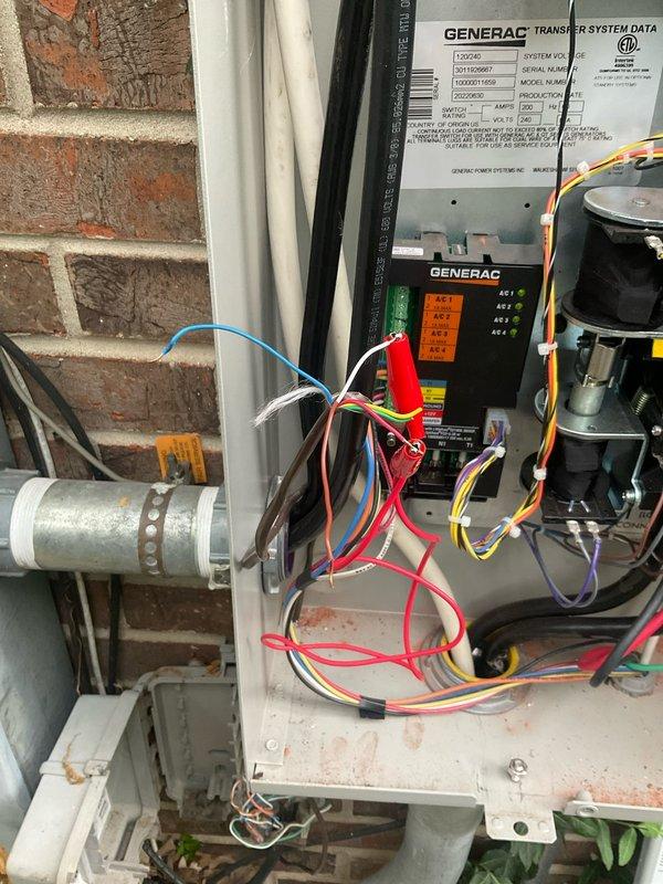 Responded to after hours service call for Generac transfer switch system inspection. Upon arrival, documented existing electrical installation mounted on exterior brick wall showing transfer switch control panel with multiple indicator lights and wire connections. Observed wiring configuration with various colored conductors (red, white, blue, yellow, orange, black, brown) routed through the system, some bundled with zip ties. Noted junction box installation on ceiling with visible wire connections secured with wire nuts. Photographed current state of equipment including control panel data plate, electrical connections, and associated components for service records. System components included transfer switch panel, cylindrical capacitor, and related electrical equipment. All observations documented for follow-up service recommendations.