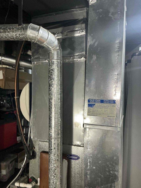 Conducted on-site evaluation of 21-year-old residential HVAC system for replacement estimate. Inspected outdoor condensing unit positioned in narrow side yard between building walls, noting age-appropriate wear on cylindrical white housing and top-mounted fan assembly. Documented refrigerant line routing and electrical connections at exterior installation.

Assessed indoor air handler unit in basement mechanical room, identifying critical operational failure evidenced by extensive frost and ice accumulation on vertical supply ductwork and unit surfaces. This severe icing condition indicates refrigerant system malfunction, likely due to low refrigerant charge, restricted airflow, or failed metering device typical of equipment at end of service life. Verified Carrier brand air handler with connected ductwork and refrigerant lines showing signs of age-related deterioration.

Provided comprehensive replacement estimate for complete HVAC system upgrade based on observed equipment age, curre