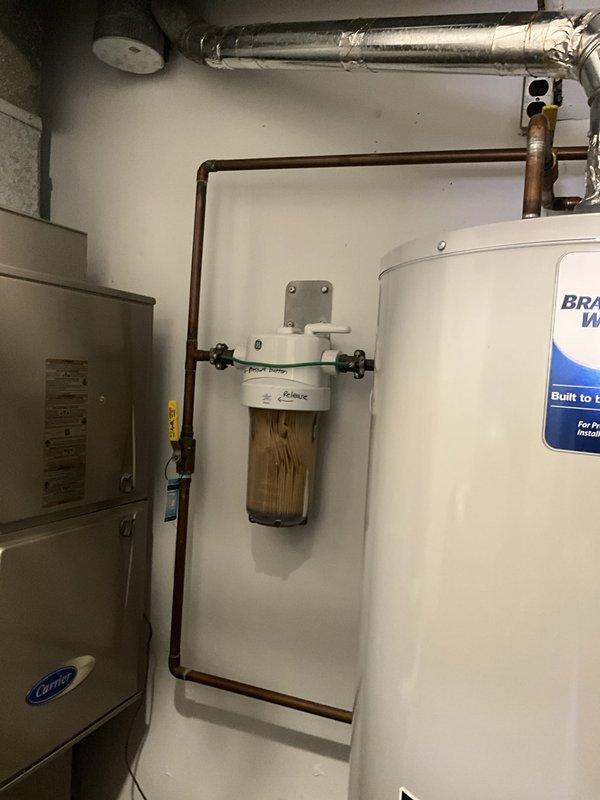 Completed comprehensive plumbing inspection as part of tune-up service, examining whole-house water filtration system with sediment filter showing normal discoloration from use, copper supply piping with bypass configuration, water heater installation, and modern bathroom shower fixture with rainfall head and handheld wand assembly. All plumbing components, connections, and fixtures were inspected and found to be functioning properly with no immediate concerns identified.