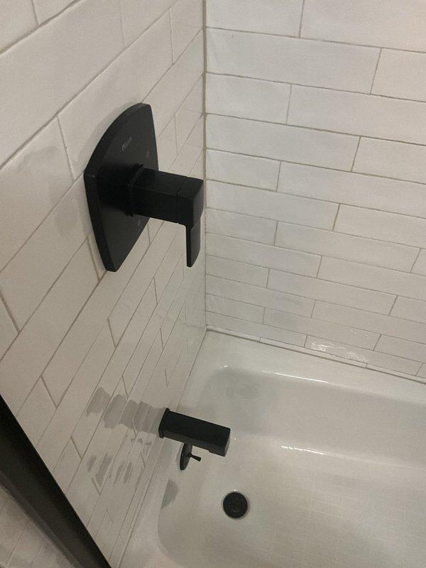 Completed installation of Pfister shower valve system and tub spout in residential bathroom. Mounted matte black single-handle shower control valve with trim kit on white subway tile wall, ensuring proper alignment and secure attachment. Installed matching black tub spout at appropriate height above tub deck. Verified water flow, tested temperature control operation, and confirmed no leaks at all connection points.