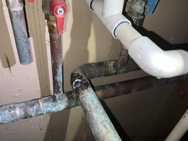 Responded to commercial tankless water heater #3 leak with active water pooling on floor. Upon inspection, identified severe corrosion and deterioration on multiple copper supply lines and connection points serving the unit. The pipes exhibited extensive blue-green copper oxidation (verdigris), heavy rust buildup, pitting, and material degradation around threaded fittings and valve assemblies. The corrosion was most concentrated at pipe joints and connections, indicating prolonged moisture exposure and age-related failure. Documented existing conditions with photographs showing the compromised plumbing infrastructure, including corroded metal pipes contrasting with newer PVC drain components in the vicinity. The leak source was traced to failed corroded connections on the water supply lines feeding the tankless unit. Immediate assessment revealed the need for comprehensive pipe replacement due to the advanced state of deterioration affecting system integrity and presenting risk of cont