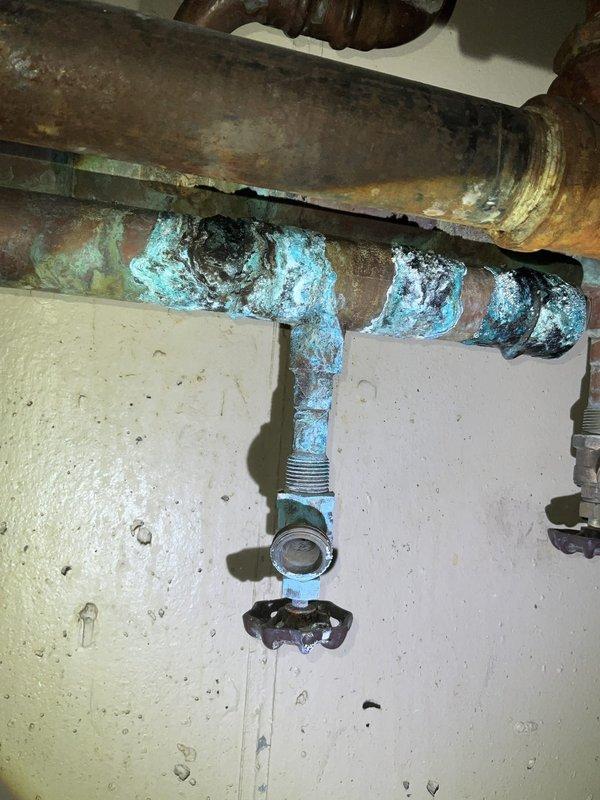 Responded to commercial tankless water heater #3 leak with active water pooling on floor. Upon inspection, identified severe corrosion and deterioration on multiple copper supply lines and connection points serving the unit. The pipes exhibited extensive blue-green copper oxidation (verdigris), heavy rust buildup, pitting, and material degradation around threaded fittings and valve assemblies. The corrosion was most concentrated at pipe joints and connections, indicating prolonged moisture exposure and age-related failure. Documented existing conditions with photographs showing the compromised plumbing infrastructure, including corroded metal pipes contrasting with newer PVC drain components in the vicinity. The leak source was traced to failed corroded connections on the water supply lines feeding the tankless unit. Immediate assessment revealed the need for comprehensive pipe replacement due to the advanced state of deterioration affecting system integrity and presenting risk of cont