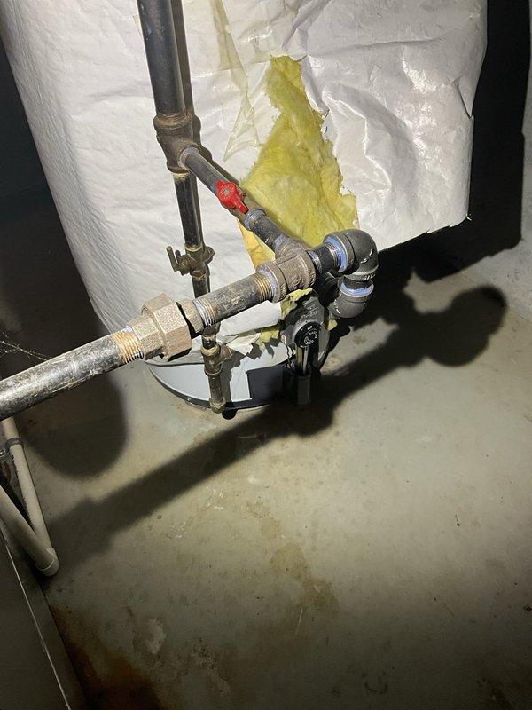 Performed comprehensive inspection of tanked water heater system exhibiting visible corrosion and aging on galvanized steel piping connections. Assessed condition of plumbing infrastructure including multiple threaded pipe joints, valve assemblies, and water heater tank insulation. Documented extensive rust formation on metal surfaces, corroded cast iron drainage piping, and deteriorating pipe fittings throughout the installation. Evaluated water heater for potential replacement due to advanced age indicators including compromised insulation jacket and oxidized connection points.