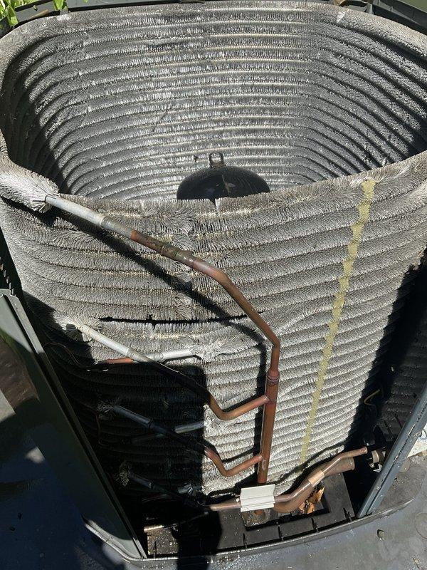 Completed comprehensive BFMA tune-up service on residential air conditioning system with equipment age exceeding six years. Performed standard maintenance protocol including system inspection, evaporator coil assessment, and refrigerant line examination. Visual inspection revealed significant dust and debris accumulation on evaporator coil assembly, with coils displaying contrasting conditions between upper and lower sections. Documented copper refrigerant lines showing surface discoloration consistent with age and outdoor exposure. System components photographed for service records, showing spiral-configured evaporator coil with multiple concentric rings and parallel fin arrangement housed within outdoor cabinet. All tune-up procedures performed according to BFMA standards with system operational upon completion.